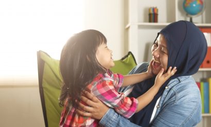 Mum and daughter laughing, with daughter putting her hands up to her mum's face