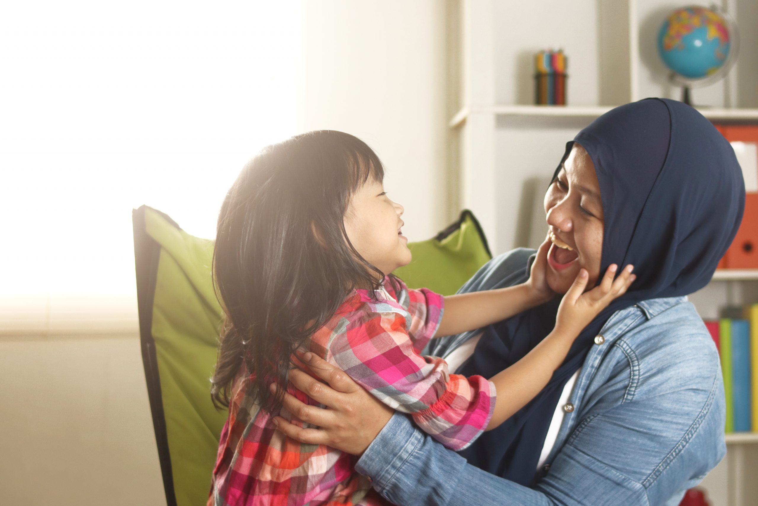 Mum and daughter laughing, with daughter putting her hands up to her mum's face